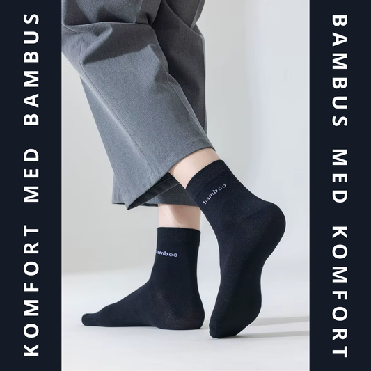 Sorte bambus strømper med hvid bamboo-tekst båret på begge fødder under grå bukser – lifestyle-foto med mørk grafisk ramme – Bambus strømper | BIBAMBUS 'Lovely Bamboo Feet'