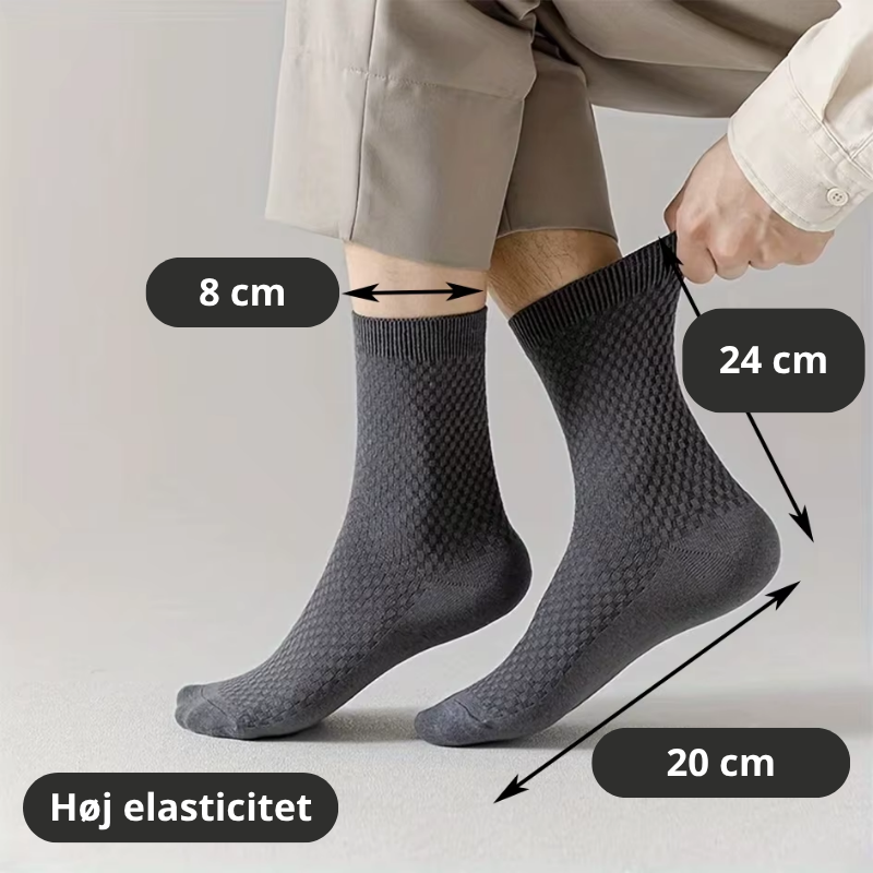 Mand der tager mørkegrå bambusstrømper på med måleangivelser: skaftbredde 8 cm, skafthøjde 24 cm og forlængde 20 cm – størrelsesguide med teksten "Høj elasticitet" – herrestrømper i bambusviskose str. 38-45 – Bambusstrømper til mænd | BIBAMBUS 'The Bamboo Gentleman'
