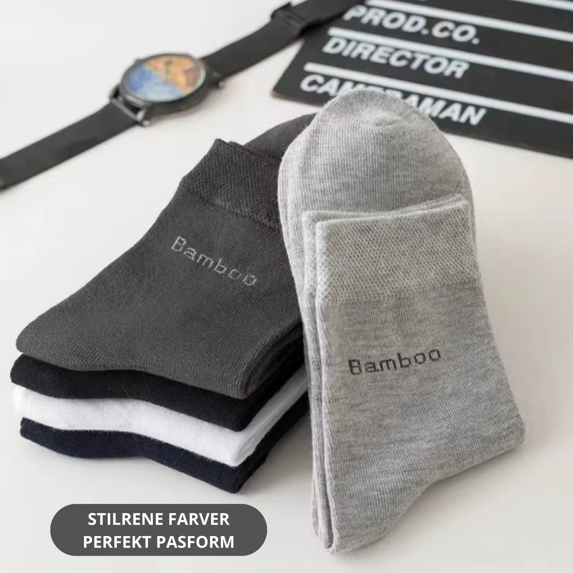 Mørkegrå og lysegrå bambus strømper med bamboo-tekst stablet og lænet mod hinanden på hvid flade med ur og filmklap i baggrunden – Bambus strømper | BIBAMBUS 'Lovely Bamboo Feet'